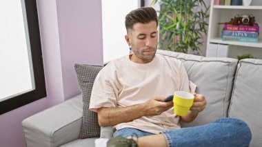 Genç İspanyol adam akıllı telefon kullanıyor. Evde kahve içiyor.