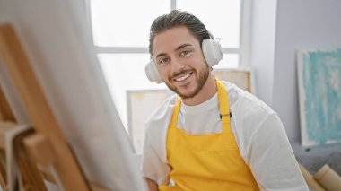 Genç İspanyol ressam resim stüdyosunda gülümseyen müzik dinliyor.