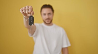 Yeni arabanın anahtarını izole edilmiş sarı arka planda tutan İspanyol genç adam.
