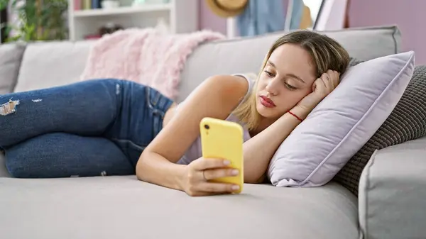 Νεαρή Ξανθιά Γυναίκα Που Χρησιμοποιεί Smartphone Ξαπλωμένη Στον Καναπέ Στο — Φωτογραφία Αρχείου