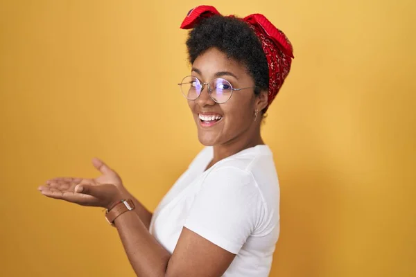 黄色の背景の上に立っている若いアフリカ系アメリカ人女性は コピースペースを示す手を開いた手のひらを脇に置き 興奮する笑顔の広告を提示します — ストック写真