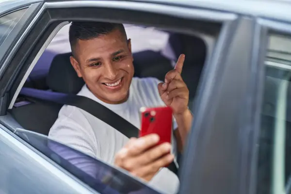 年轻的他的惊慌失措的男人用智能手机在车里做视频通话 高兴地微笑着 手指手画脚地指向旁边 — 图库照片