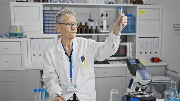 屋内実験室のテスト管の灰色髪の女性の科学者働き 測定の液体は医学研究の安全そして精密を細心に保障します — ストック写真