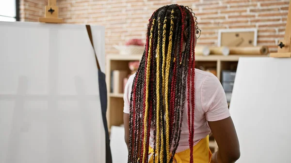 African american artist - a woman of power, standing back to easel at her indoor art studio, baring her braids and passion for painting