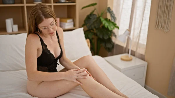 ベッドに座っている若い金髪の女性は寝室で脚にスキン治療を適用セクシーに見えます — ストック写真