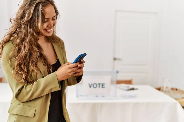 Young beautiful hispanic woman voter using smartphone at electoral college