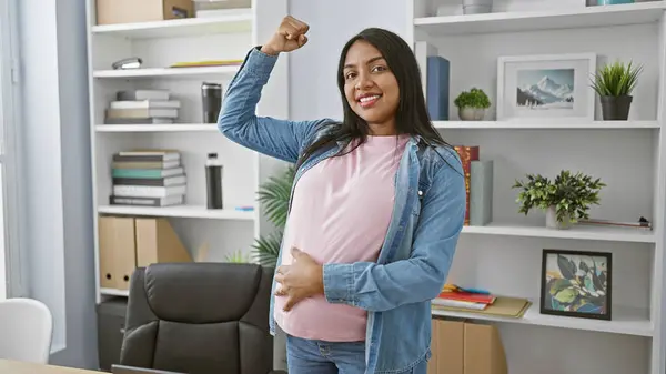 年轻的孕妇面带微笑 有自信的生意人 以坚定的姿态显示力量 在办公室里摸她的肚子 看着相机 享受她的母性和成功 — 图库照片