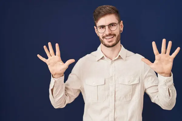 青い背景の上に立っているひげを持つヒスパニック男性は自信と幸せを笑いながら指ナンバー10を指で指で指摘します — ストック写真