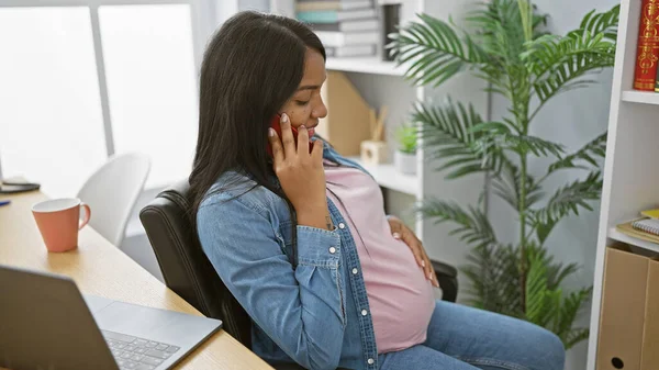 当她在办公室里放松时 这位成功的年轻而恐慌的怀孕女商人一边用智能手机边笑 一边轻柔地摸着自己的肚子 — 图库照片