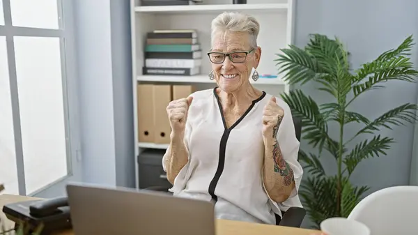 優雅な灰色の髪のシニア女性 笑顔のビジネスワーカーは 勝利のジェスチャーで交差したラップトップのオフィスデスクで仕事の勝利を祝います — ストック写真