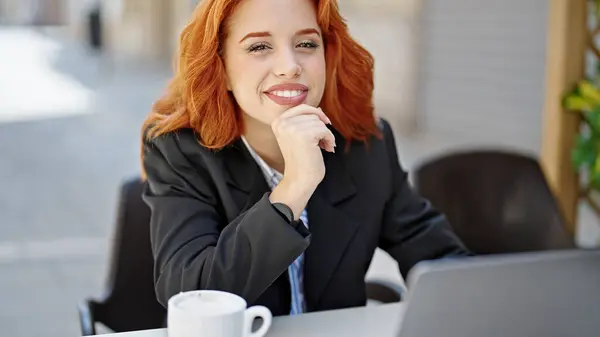 Young redhead woman business worker using laptop smiling at coffee shop terrace