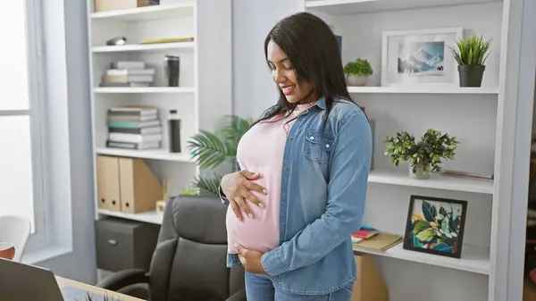 年轻孕妇在办公室工作时 满脸笑容自信地摸着肚子 体现了母性和商业上的成功 — 图库照片