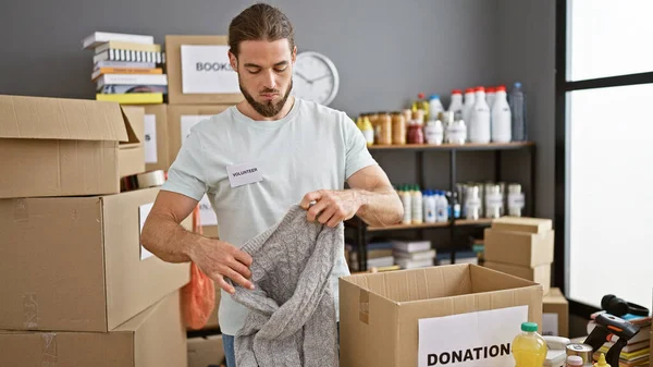 Young hispanic man volunteer packing clothes on cardboard box at charity center