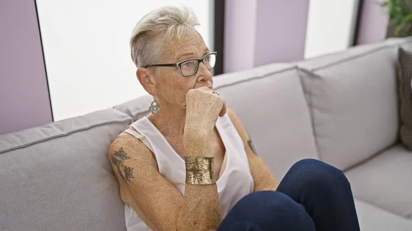Starsza Siwowłosa Kobieta Zanurzona Głębokiej Refleksji Siedząc Wygodnie Przytulnej Sofie — Zdjęcie stockowe