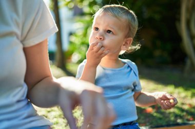 Anne ve oğlu bankta oturup parkta küçük solucanlar yiyorlar.