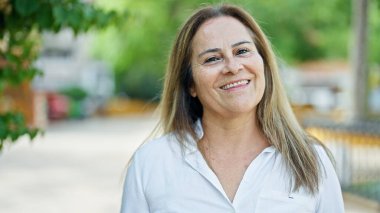 Middle age hispanic woman smiling confident standing at park