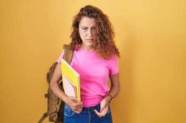 Öğrenci çantası takan, elinde kitap tutan, kuşkucu ve gergin genç beyaz bir kadın sorun yüzünden surat asıyor. negatif kişi. 