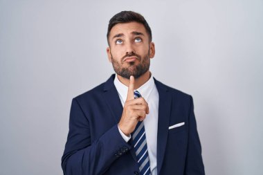Yakışıklı İspanyol takım elbiseli ve kravatlı adam şüpheye odaklanmış, çenesinde parmak olan ve kafasını kaldırıp merak eden. 