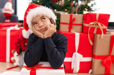 Sevimli İspanyol çocuk elinde noel hediyesi tutarak evde mutsuz bir ifadeyle yerde oturuyor.
