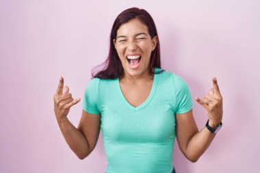 Genç İspanyol kadın pembe arka planda duruyor çılgın bir ifadeyle bağırıyor elleri havada rock sembolü yapıyor. Müzik yıldızı. ağır müzik konsepti. 