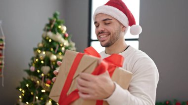 Evde kendine güvenen genç İspanyol adam Noel hediyesini tutuyor.