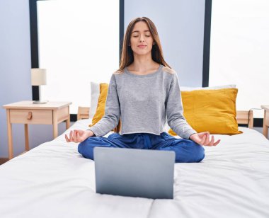 Genç ve güzel İspanyol kadın yatak odasında oturmuş yoga yapıyor.
