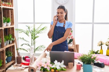Young beautiful hispanic woman florist talking on smartphone working at florist