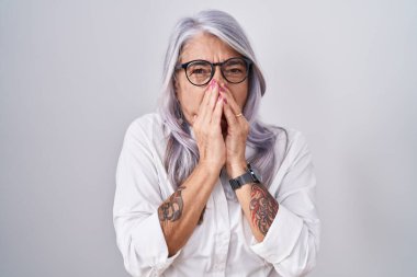 Beyaz arka planda duran gözlüklü, orta yaşlı bir kadın pis ve iğrenç bir koku alıyor, nefesini burnunda tutuyor. Kötü kokuyor. 