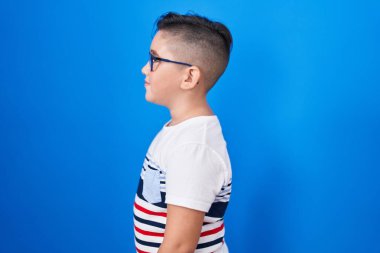 Genç İspanyol çocuk mavi arka planda duruyor. Yan tarafa bakıyor, rahat poz veriyor. Kendine güvenen bir gülümsemesi var.. 