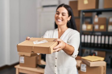 Young beautiful hispanic woman ecommerce business worker holding package at office