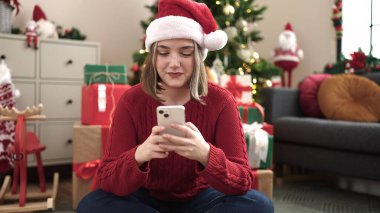 Evdeki Noel ağacının yanında akıllı telefon kullanan genç sarışın kadın.