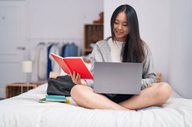 Genç Çinli kadın dizüstü bilgisayar kullanıyor. Yatak odasında ders çalışıyor.