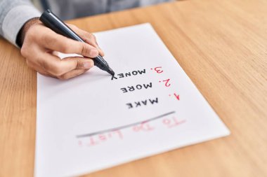 Young hispanic man writing to do list on paperwork at office