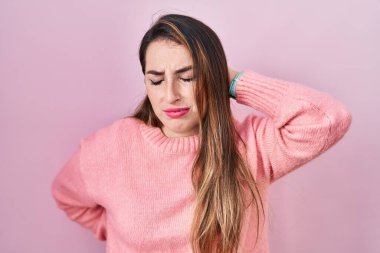Young hispanic woman standing over pink background suffering of neck ache injury, touching neck with hand, muscular pain 