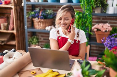 Çiçekçide dizüstü bilgisayarla konuşan sarışın bir çiçekçi.