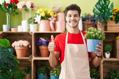 Çiçekçi dükkanında çalışan genç İspanyol adam elinde mutlu ve olumlu bir gülümseme, başparmağıyla mükemmel ve onay işareti yapıyor. 