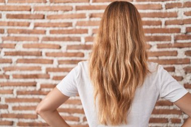 Kafkasyalı genç bir kadın tuğla duvarın üzerinde dikiliyor geriye bakıyor kollarını vücuduna dikiyor. 