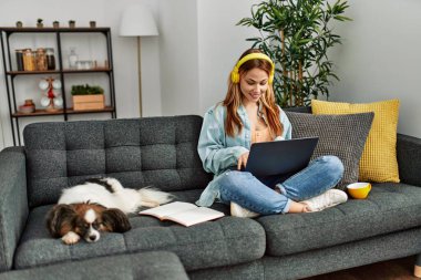 Kanepede oturan beyaz bir kadın ve evde ders çalışan bir köpek.