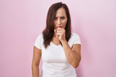 Orta yaşlı esmer kadın pembe arka planda dikiliyor kendini iyi hissetmiyor ve soğuk algınlığı veya bronşitin belirtisi olarak öksürüyor. sağlık hizmeti kavramı. 