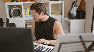 Young hispanic man musician playing piano at music studio
