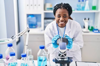 African american woman scientist smiling confident using microscope at laboratory