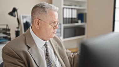 Ofiste çalışan bilgisayar kullanan, orta yaşlı, kır saçlı bir iş adamı.