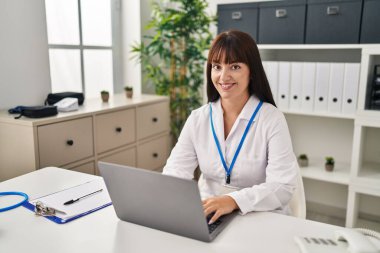 Genç, güzel İspanyol kadın doktor klinikte laptopunu kullanıyor.