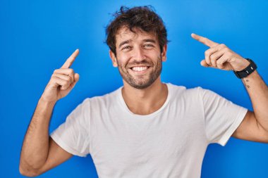 Hispanic young man standing over blue background smiling pointing to head with both hands finger, great idea or thought, good memory 