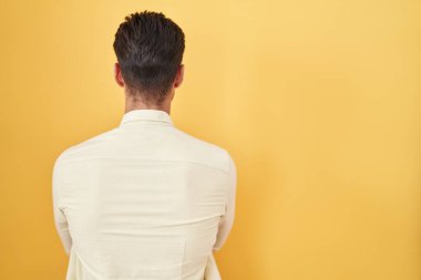 Sarı arka planda dikilen İspanyol genç adam çapraz kollarla diğer tarafa bakıyor. 