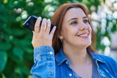 Young beautiful plus size woman smiling confident listening audio message by the smartphone at park
