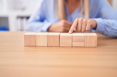 Young blonde woman business worker sitting on table with wooden cubes at office