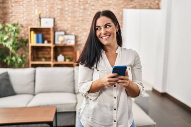 Genç, güzel, İspanyol bir kadın evde akıllı telefon kullanıyor.