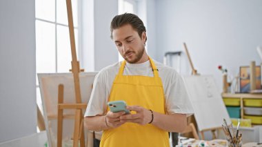 Genç İspanyol ressam sanat stüdyosunda akıllı telefon kullanıyor.
