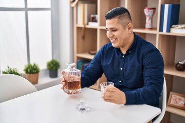 Genç latin adam evdeki masada oturmuş viski içiyor.